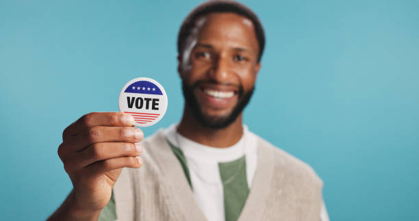 istock Black man, vote badge and politics in studio, platform support and message for election registration. Male person, patriotic representative and pin on blue background, campaign volunteer and portrait 2203034201
