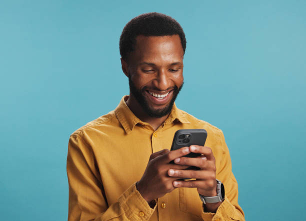 istock Online, black man and happy with typing on smartphone in studio for text message, internet search and playing games. Mockup space, person and smile with phone for streaming service on blue background 2203034247