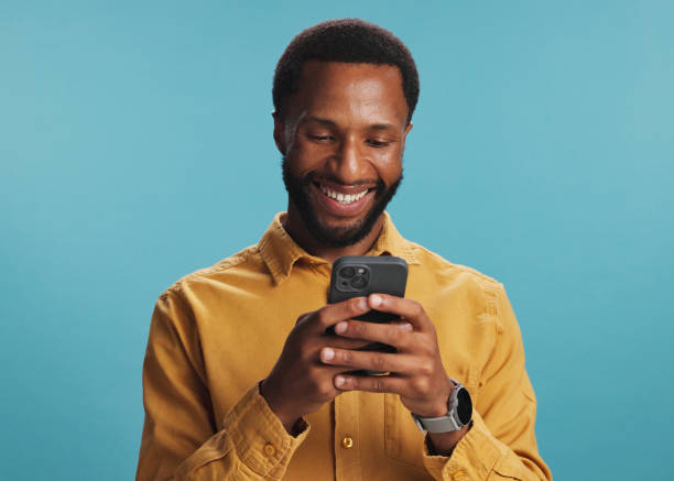 istock Black man, phone and happy with typing in studio for text message, internet search or playing online games. Mockup space, person and smile with smartphone for communication or chat on blue background 2203034249