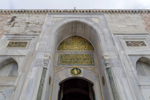 A bright and captivating view of the Imperial Gate (Bab-üs Selam) of Topkapi Palace in Istanbul, Turkey, captured on a clear summer day. The iconic twin towers, historic Ottoman stone architecture, and the Turkish flag standing proudly above the wall create a strong visual symbol of heritage and national identity. Soft sunlight enhances the warm texture of the stone, while surrounding trees add a natural frame and a sense of serenity.