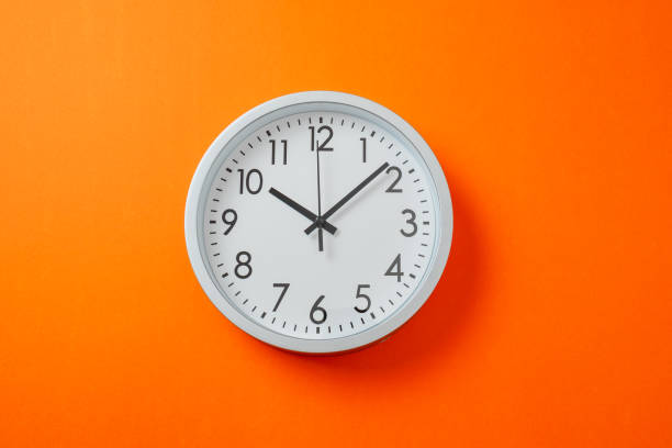 istock Round clock shows time 10 hours ten minutes. Clock on hot orange background. 2203035235