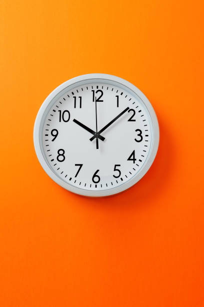 istock Round clock shows time 10 hours ten minutes. Clock on hot orange background. 2203035297