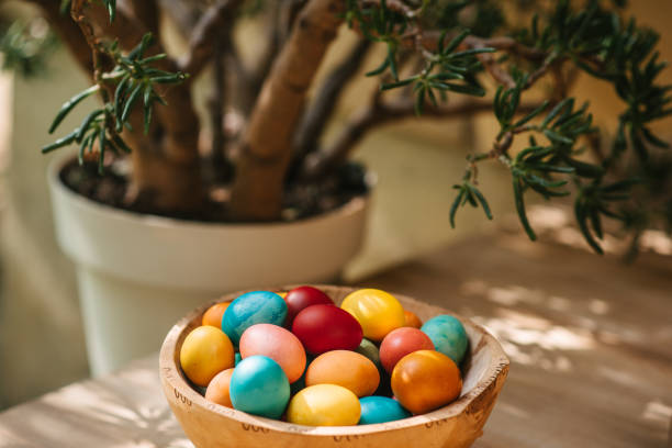 Colorful Easter eggs in wooden bowl next to a plant