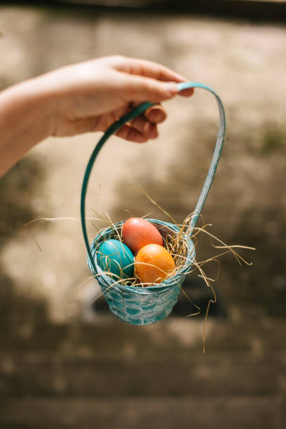 A close-up of a hand holding a small basket filled with vibrant, multicoloured Easter eggs
