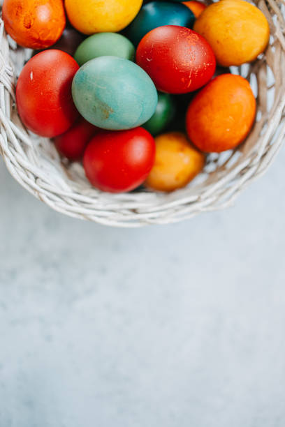 A variety of vibrant Easter eggs placed in a rustic wooden basket on light background