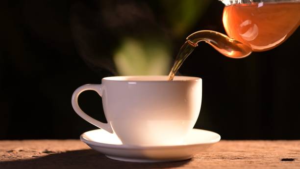 istock Pouring fresh tea into a white cup on a wooden table surrounded by nature captured in soft lighting evoking calmness and serenity 2203039696