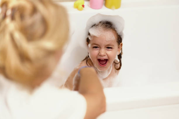 A mother bathes her little happy daughter in a bubble bath