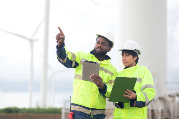 istock Two engineer check and examining wind turbines in wind farm, renewable energy and teamwork in a sustainable environment, inspection power electric with document and tablet, industry and eco. 2203043214