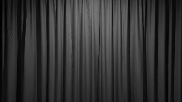 A luxurious, textured dark black fabric curtain, draped in soft folds and illuminated with a subtle glow, creates an elegant and versatile background suitable for stage curtains.