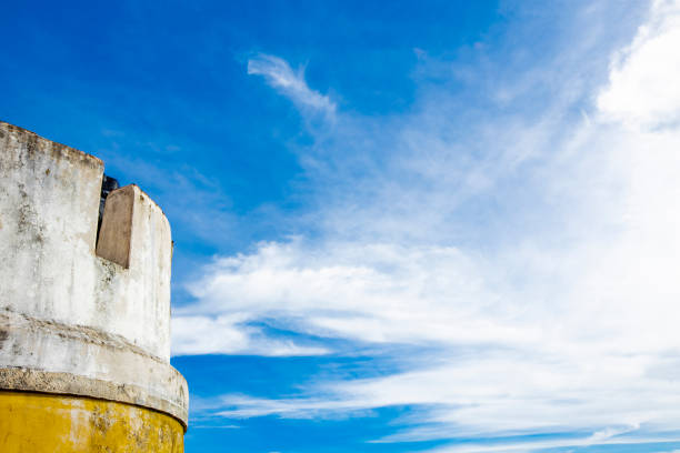 A beautifully weathered fort wall stands majestically against a backdrop of bright blue sky and fluffy white clouds, creating a serene atmosphere.