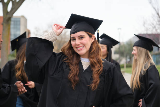 istock Happy graduating student adjusting her mortarboard with classmates in the background 2203048697