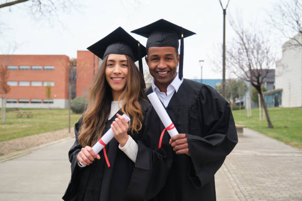 istock Two happy students smiling and holding diplomas at graduation ceremony 2203050100