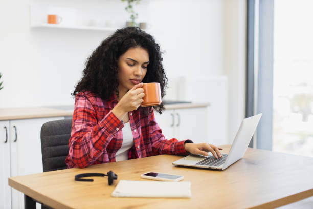 istock Woman working on laptop while drinking coffee in cozy office environment 2203052215