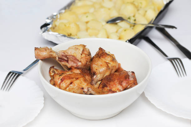Roasted chicken in bowl. White plates and tray of potatoes.