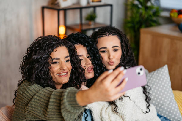 istock Three Curly Sisters Taking Selfies Using A Smart Phone On The Sofa At Home At Night 2203054811