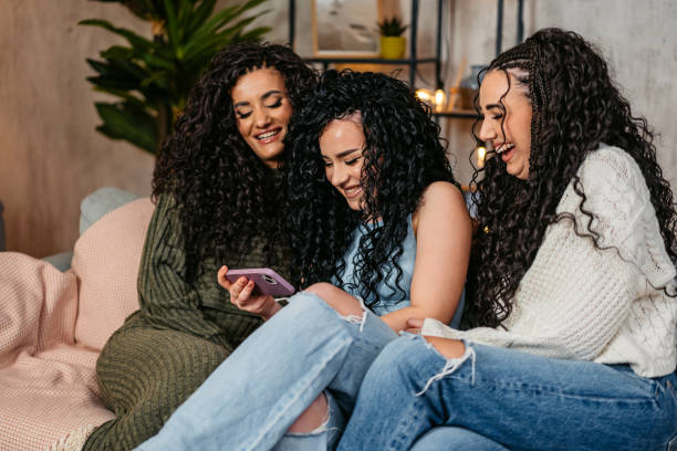 istock Three Curly Sisters Using A Smart Phone Together On The Sofa At Home At Night 2203055127