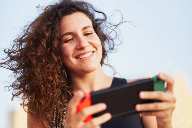 istock Woman playing video games with handheld console outdoors and smiling 2203056215