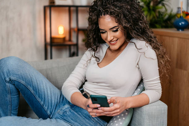 istock Young Curly Woman Using Her Smart Phone On The Sofa At Home At Night 2203056232