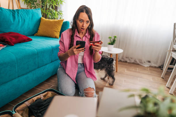 istock Woman using smartphone and credit card while packing a suitcase at home 2203063391