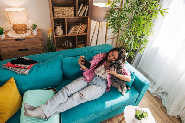 istock Young woman relaxing on sofa with dog and packing suitcase 2203064359