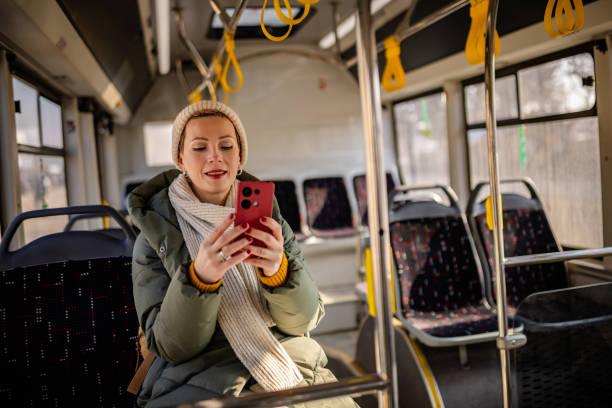 istock Cheerful young woman enjoying a bus ride in a vibrant urban setting while using her smartphone 2203064656