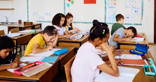 istock Multiracial school children sitting at desks in classroom, concentrating on making notes 2203067266