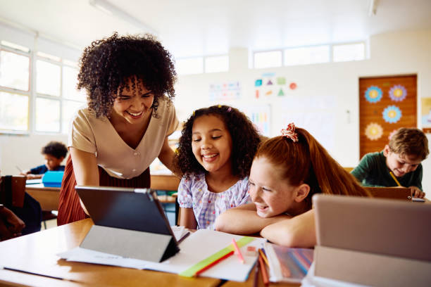 istock Young female teacher talking to schoolgirls using digital tablet in class, laughing 2203067363