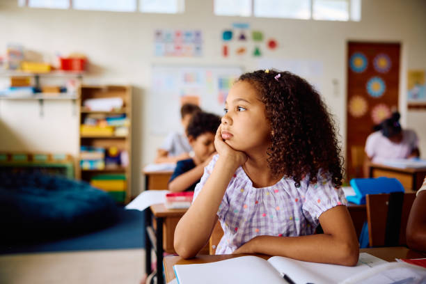 Schoolgirl sitting in class, resting elbow on desk and looking sideways, daydreaming