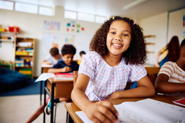 istock Elementary schoolgirl sitting at desk, smiling happily at camera in class 2203067508