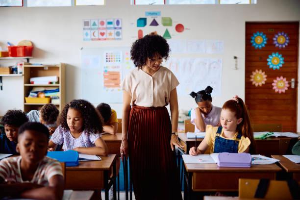 istock Elementary school teacher looking at schoolgirl's work in class 2203067575