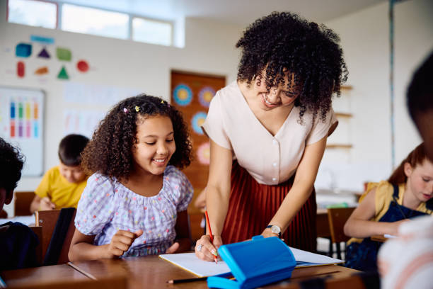 istock Cheerful elementary school teacher helping schoolgirl in classroom 2203067581