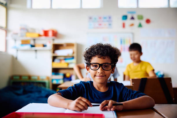 istock Schoolboy sitting at desk, smiling at camera 2203067597