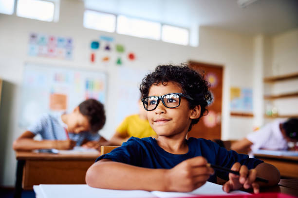Schoolboy sitting at desk, smiling, looking sideways stock photo