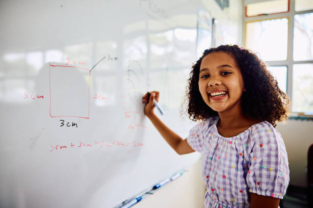 istock Schoolgirl writing on whiteboard, looking sideways at camera, smiling in class 2203067622