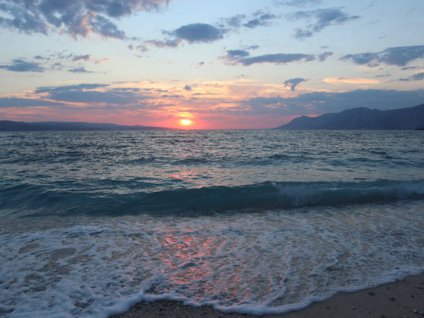 Bright sun at sunset over the sea is reflected in the sea foam, sand and wet stones on the shore.
