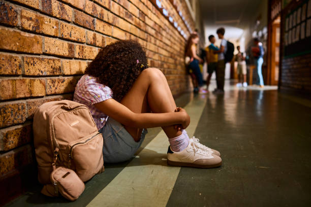 istock Schoolgirl leaning on wall, hiding head between legs in school corridor 2203067763