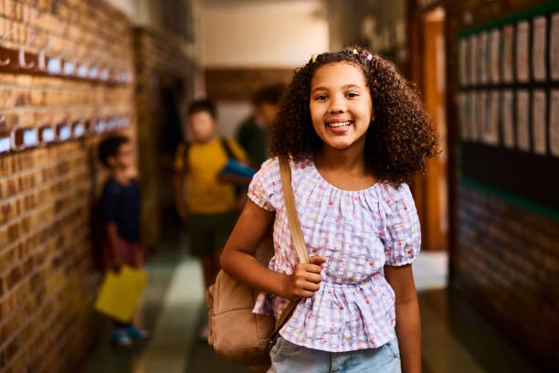 istock Cheerful elementary schoolgirl smiling happily at camera in school corridor 2203067794