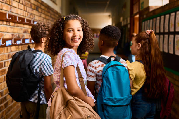 istock Schoolgirl looking over shoulder, smiling at camera in school corridor 2203067795