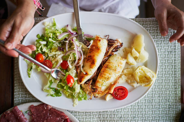 Two perfectly grilled squids served alongside a vibrant fresh salad, tender boiled potatoes, and a zesty slice of lemon, inviting diners to indulge in a mediterranean culinary experience