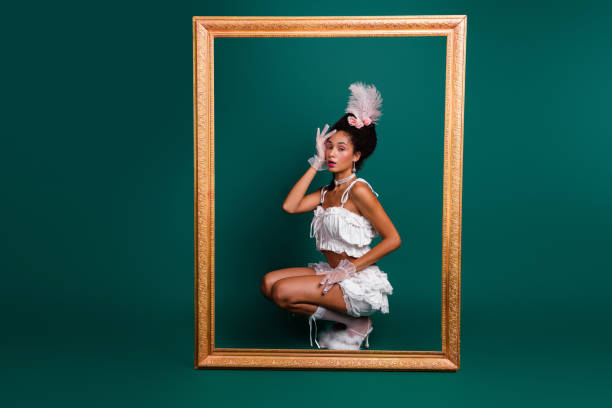 A young woman poses playfully within a golden frame against a green backdrop, showcasing a blend of vintage and modern style