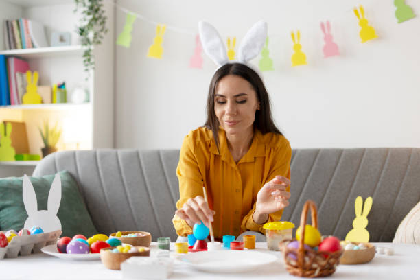 istock Woman painting easter eggs at home wearing bunny ears 2203071755