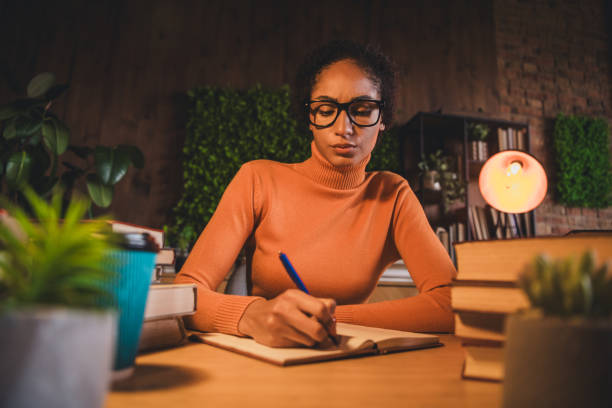 istock Young woman in a cozy home setting studying with focus and dedication in the evening, surrounded by plants and book 2203071967