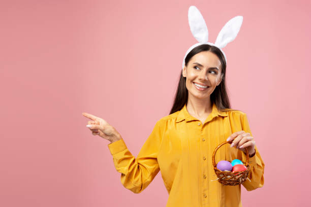 istock Woman pointing with easter bunny ears holding basket with colored eggs 2203072188