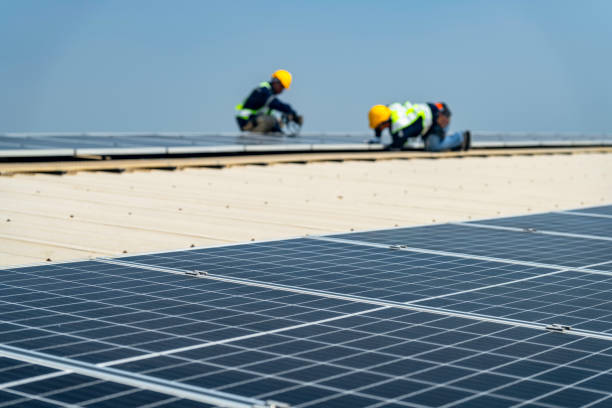 istock Two engineers install solar panels on a rooftop, wearing safety gear and helmets. The scene showcases renewable energy, green technology, and sustainable solutions under a clear blue sky. 2203072599