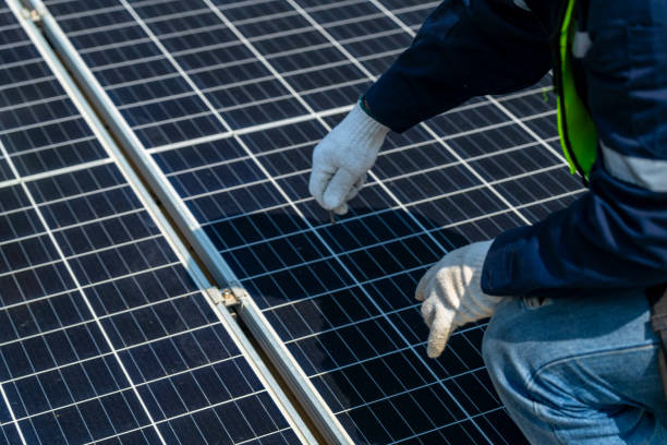 istock Two engineers install solar panels on a rooftop, wearing safety gear and helmets. The scene showcases renewable energy, green technology, and sustainable solutions under a clear blue sky. 2203073645