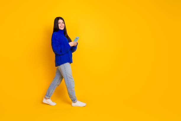 istock Young woman in a blue pullover holding a phone against a yellow background 2203077897