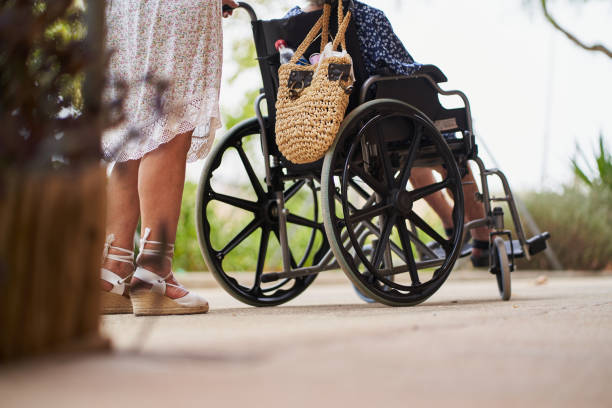 Daughter pushing her elderly mother in a wheelchair, enjoying a sunny day together in a park, demonstrating love, care, and support for her aging parent