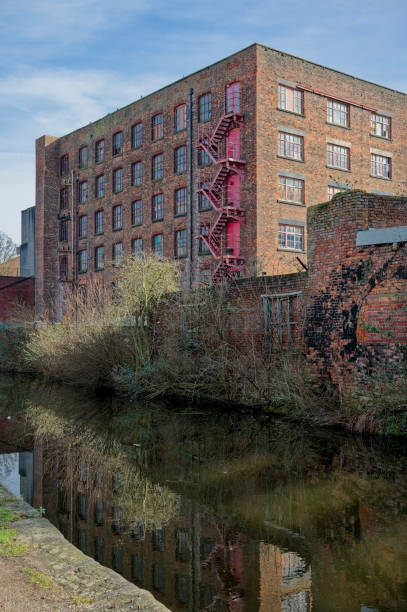 istock Historic brick mill building with red fire escape beside a calm canal. 2203086881