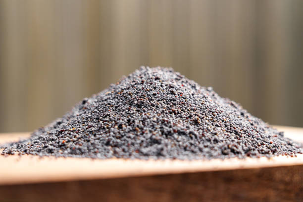 Poppy seeds on wooden surface. Delicate grains forming a soft mound against a blurred background.