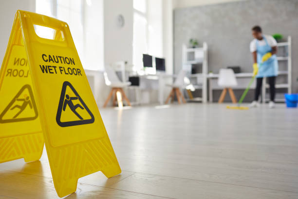 istock Caution sign warning us of wet floor placed by cleaner who's working in background 2203094149